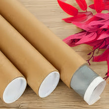 Load image into Gallery viewer, Rolled tube packaging for canvas prints laid on a wooden surface with pink decorative leaves.
